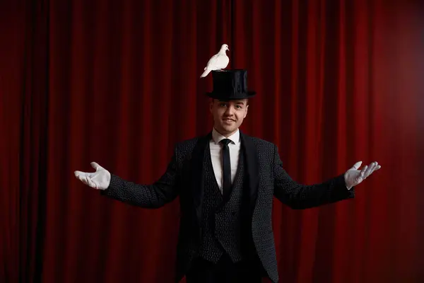 美しい白い鳩の鳥とトリックを行うマジシャンは劇的な劇場ステージの赤いカーテンの上に立っている彼の魔法のスキルを示しています ストックフォト
