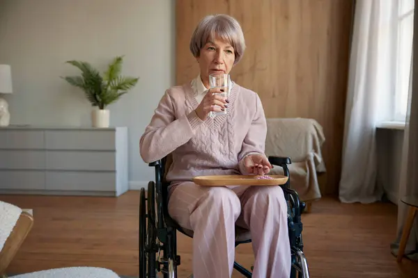 ホスピスでリハビリとヘルスケアのための処方薬を取る車椅子の孤独な悲しい老婆 ストック画像