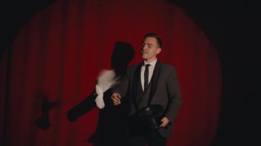 Sihirbaz adam güzel beyaz güvercin kuşuyla numara yapıyor sihirli yeteneklerini sergiliyor dramatik tiyatro sahnesinin kırmızı perdesinin önünde duruyor.