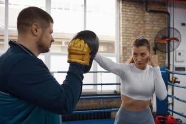 Spor salonunda erkek antrenörüne yumruk atan atletik bir kadın. Kendini koruma ve kendini savunma konsepti için spor ve kadın dövüş sanatları.