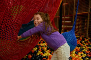 Küçük anaokulu kızı oyun merkezinde neşeli ve eğlenceli vakit geçiriyor. Gülen kız çocuk top havuzunda saklambaç oynuyor. Kreş kulübünde eğlence zamanı.