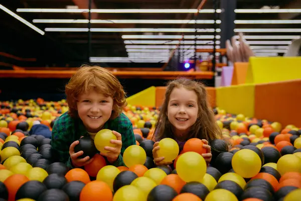屋内遊び場でアクティブな楽しい時間を楽しむカラフルなプラスチックボールとドライプールに横たわる面白い子供たちを魅了します 幸せな子供時代と興奮する休日 ストック写真