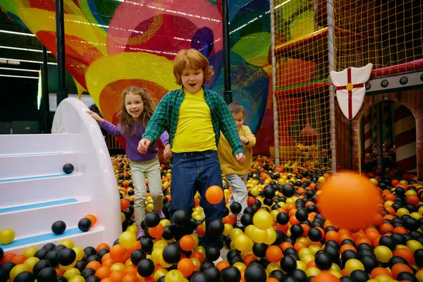 令人惊奇的无忧无虑的学龄前儿童一起在室内操场上玩彩色塑料球 儿童放松游戏中心的安全吸引设备 图库图片