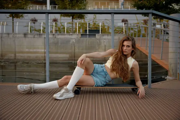 年轻女子穿着休闲少女的衣服 在滑板上摆着姿势 都市文化 自由风格 现代青少年一代 图库图片