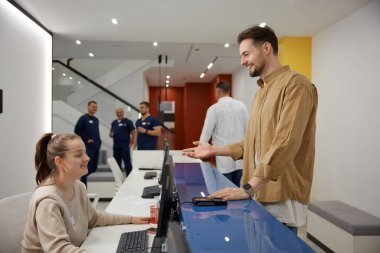 Tıbbi klinik bekleme odasındaki hemşire ile konuşan ve gülümseyen bir adam. Erkek hasta doktordan randevu alıyor.