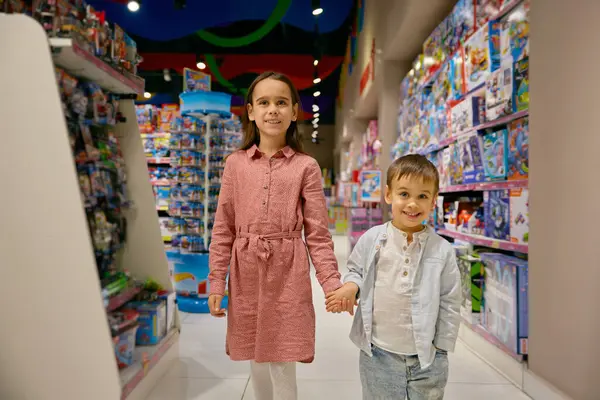 高兴的小孩带着玩具走在陈列柜中 可爱的女孩和男孩一起在超级市场挑选玩具 — 图库照片