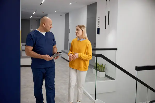医師と女性の患者は 診療所の廊下に立っている間に何かを議論しています 女性訪問者に無料で相談できるプラクティショナーセラピスト 医学と医療のコンセプト — ストック写真