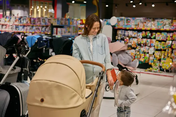 快乐快乐的怀孕母亲和小儿子选择婴儿车作为新家庭成员的商店 免版税图库照片