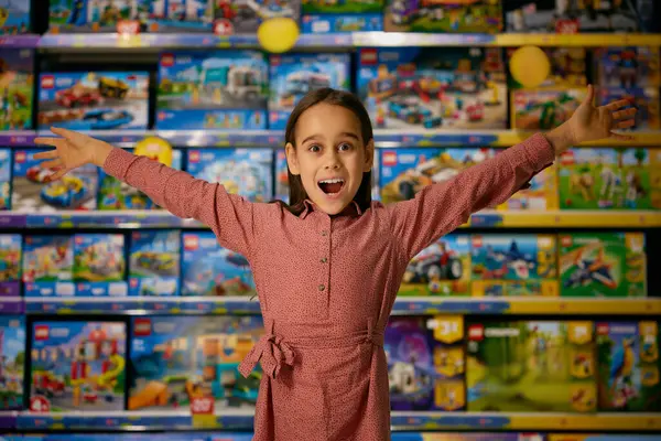 一个带着玩具陈列柜站在商场后面的小女孩惊讶的画像 小孩在商店里期待着买东西时 心里充满了积极的情绪和尖叫 图库照片