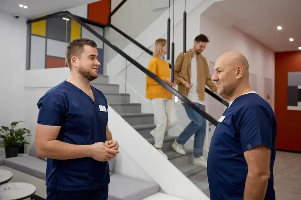 两名身穿制服的男医生在现代诊所大厅里交谈 工作沟通 从业人员对话概念 免版税图库图片