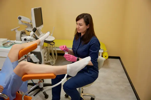 医生在妇科椅上为女病人提供检查 女妇科医生戴手套 手持无菌器械 进行专业诊断 生育率中心 图库图片