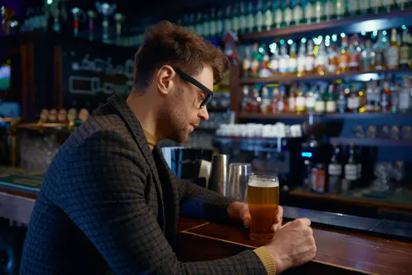 沉思的 放松的 微笑的商人在酒吧里拿着一杯冰凉的泡沫啤酒 周五晚上工作后休息一下 免版税图库图片