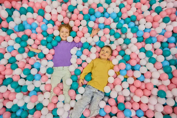 孩子们喜形于色的躺在一个巨大的干水池里 头顶上是一个五彩缤纷的塑料球 儿童派对假期在室内娱乐中心举行 图库图片