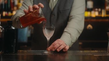 Barmen, bar tezgahında geleneksel kokteyl bardağıyla alkollü içki süslüyor. Barmen, gece kulübünde müşteriye çok yönlü içecek servisi yapıyor. Yakın görünüm