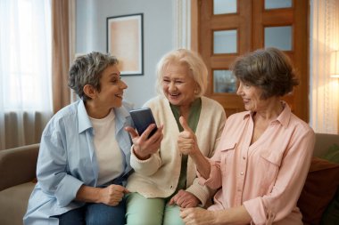 Akıllı telefon ekranına bakan emekli kadınlar. Yaşlı bayanlar eğlenceli videolardan hoşlanıyorlar ya da sosyal medyada arkadaşlarıyla internetten konuşuyorlar. Kadın arkadaşlık topluluğu.