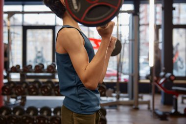 Spor salonunda halterle vücut geliştirme antrenmanından zevk alan kendinden emin bir öğrenci. Çocuklar için sağlıklı etkinlik