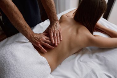 Kadın kas ağrısı için osteopatik sırt masajı yaptırıyor. Profesyonel terapi uygulayan erkek terapist müşterinin omurgasına masaj yapıyor.