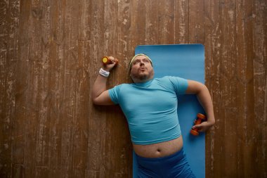 Spor antrenmanından sonra kendini yorgun hisseden komik şişman adam. Kilo kaybı ve kas gelişimi için umbellerle fiziksel egzersiz