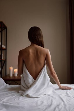 Havluya sarılı genç ve güzel bir bayan müşteri kanepeye oturmuş masaj seansından sonra spa ve sağlık merkezinde dinleniyor.