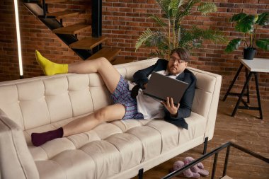 Şaşırmış iş adamı, evde oturma odasındaki kanepede oturmuş bilgisayarın ekranına bakıyor. Bilgisayar kullanarak e-posta haberlerini okuyan kafası karışmış pazarlamacı girişimcisi