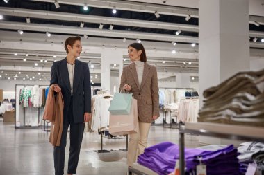 Büyük moda mağazasında alışveriş yapan mutlu genç bayan arkadaşlar. İndirim ve satış konseptiyle satın almalar
