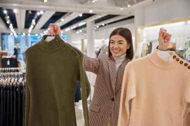 Askılarda yeni örülmüş süveter tutan mutlu bir kadının portresi. Bir fiyatına iki tane, indirimli alışveriş konsepti.