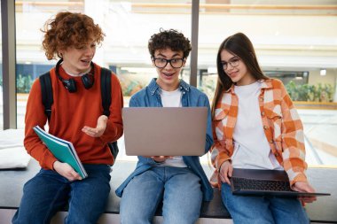 Ofiste oturup dizüstü bilgisayara bakan üç genç birlikte çalışmalarını tartışıyor. Modern ortak çalışma binasındaki adamlar