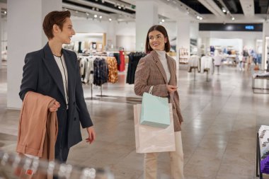 Büyük moda mağazasında alışveriş yapan mutlu genç bayan arkadaşlar. İndirim ve satış konseptiyle satın almalar