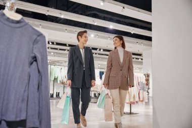 Genç bayan arkadaşlar büyük bir moda mağazasında birlikte alışveriş yapıyorlar. İndirim ve satış konseptiyle satın almalar