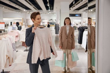 Kadın arkadaşlar büyük bir moda mağazasında birlikte alışveriş yapıyorlar. İndirim ve satış konseptiyle satın almalar