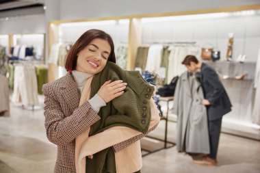 Mutlu bir kadının portresi askılarda yeni örülmüş süveterler tutuyor. Bir fiyatına iki tane, indirimli alışveriş konsepti.