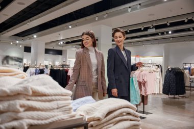 Şirin kızlar moda mağazasından alışveriş yaparken gülümseyen sıradan örgü kazaklar seçiyorlar.