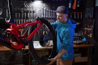 Hippi bisikletli tamirci, garaj atölyesinde arka tekerleği sökmekle meşgul.