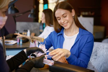 Mutlu kadın müşteri manikür için renk paletinde oje seçiyor. Güzellik salonundaki profesyonel manikürcüden konsültasyon alıyor.