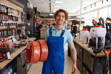 Hırdavatçıdan değiştirilebilir hortum malzemesi alan adam. Perakende satış mağazasından alışveriş yaparken hortumlu rulo taşıyan erkek işçi.