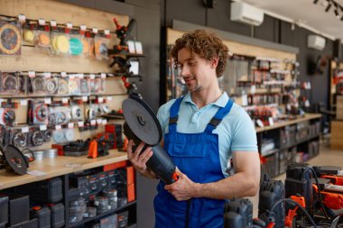 Hırdavatçıda büyük açılı değirmeni test eden bir işçi. Satılık endüstriyel elektrikli aletleri sergileyen mağaza asistanı