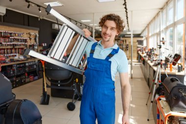 İnşaatçı hırdavatçıdan yüksek binalar için çelik merdiven alıyor. Tamirci, DIY mağazasında inşaat merdivenlerini seçiyor.