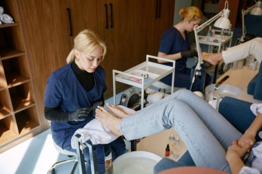 Üniformalı kadın pedikür uzmanı tırnak tırnağını törpüleme fırçasıyla törpülüyor. Güzellik salonunda ya da manikür stüdyosunda güvenlik ve konfor hizmeti