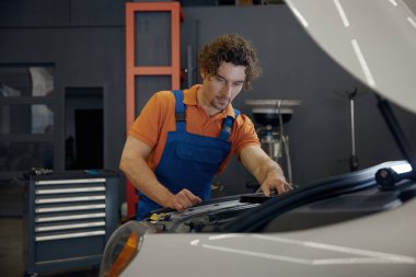 Araba kaputunun altına bakan erkek tamirci motor kontrolü yapıyor. Otomatik tanı ve onarım hizmeti kavramı