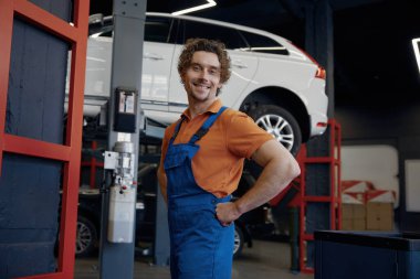 Araba tamir atölyesinde kameraya poz veren, üniformalı profesyonel bir tamirci.