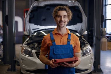 Tamir istasyonunda otomobil arızası ile uğraşırken bilgisayar tabletine bakan erkek araba teknisyeni