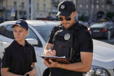 Devriye polisi park halindeki arabalarla şehir caddesinde çalışıyor. Polis memurları sokakta çalışıyor..
