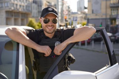 Şehrin arka planında üniformalı, gülümseyen cesur devriye arabasının portresi. Profesyonel şehir trafik koruma servisi.