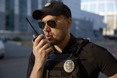 Devriye gezen erkek polis memurunun yakın plan portresi trafik istikrarını ve şehir sokaklarındaki hukuka uyumu izlerken telsizle konuşuyor.