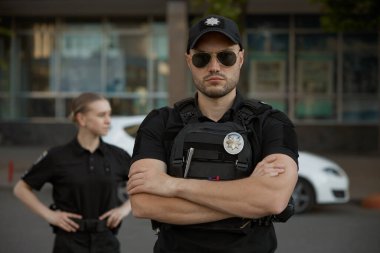 Arka planda bulanık duran genç bir kadın polisle birlikte çok cesur bir polis memurunun portresi. Profesyonel polis gücü ve şehir güvenlik görevlisi.