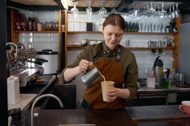 Kahveci kadın elleri bardağa süt dolduruyor. Cappuccino içecek hazırlığı ve restoran veya kafeterya hizmeti konsepti