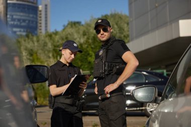 Devriye polisi park halindeki arabalarla şehir caddesinde çalışıyor. Polis memurları sokakta iş başında. Sokak güvenliği ekibi iş başında.