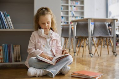Modern şehir kitapçısının zemininde kitap okuyan şirin meraklı küçük kız çocuğu. Çocuklar için halk kütüphanesinde vakit geçirirken çocuk gazete okuyor. Eğitim kavramı