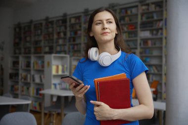 Telefondaki e-posta mesajlarını okuyan genç bir kadın kütüphanenin iç mimarisi üzerine çalışmak için kitap okuyordu.