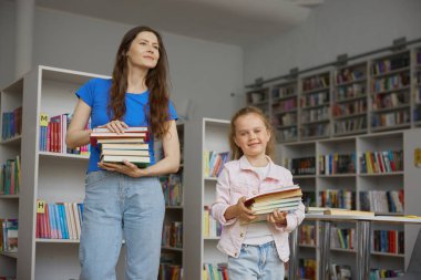 Mutlu aile kitapçıda alışveriş yapıyor. Anne ve kızı kitap taşıyarak eğitime hazırlanıyorlar.